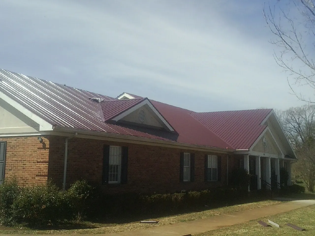 Red metal roof with gabled entries on a long brick building, from a Hail Damage Roof Repair job in Parowan