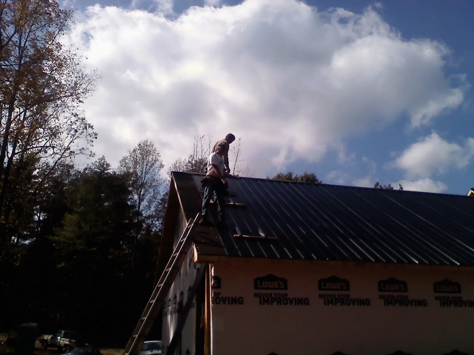 Roofer fastening dark metal panels high against a cloudy sky, from a Roof Inspection job in Parowan