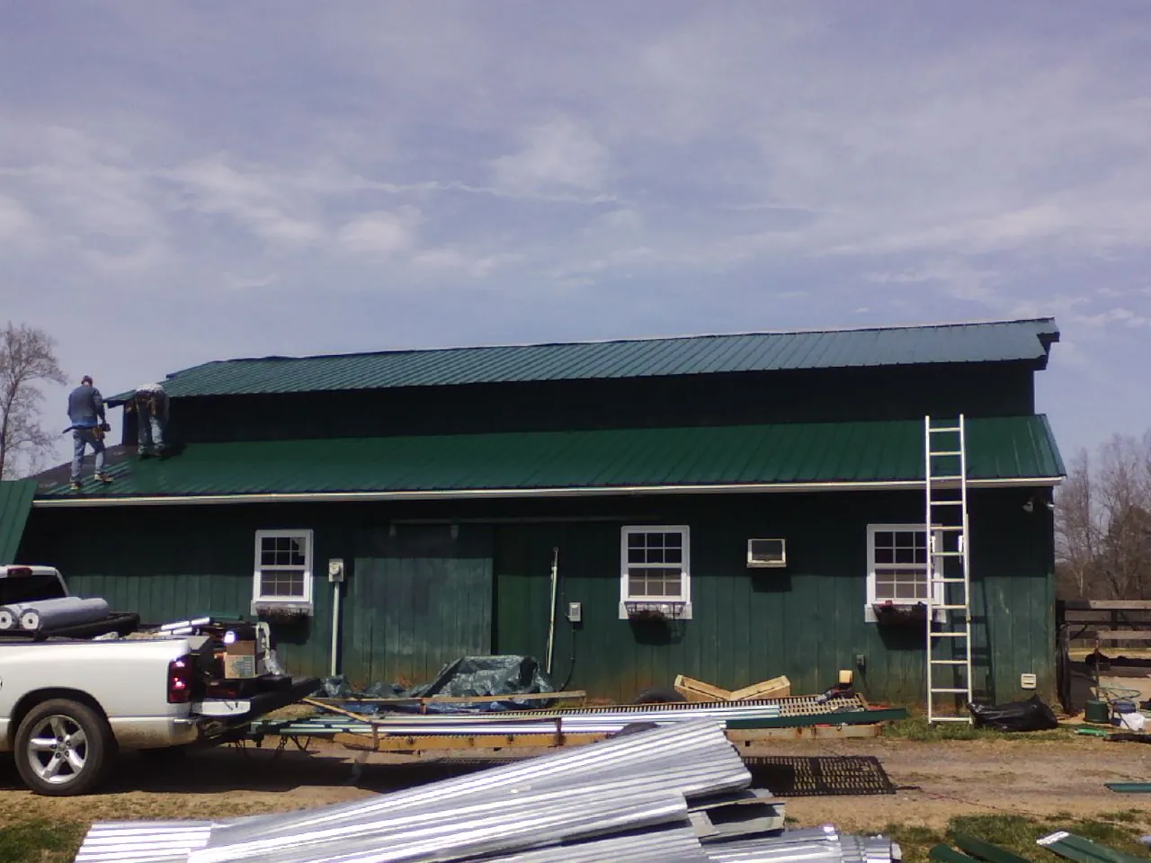 Crew installing green metal roofing on a large green barn in Parowan